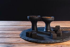 Coals, tweezers and hookah bowls on wooden surface isolated on black