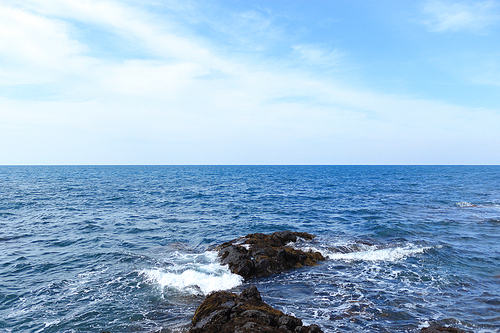 제주도에서 현무암 돌위에서 부딪히는 하얀파도와 푸른빛깔 바다의 수평선과 맞닿은 맑고 푸른하늘