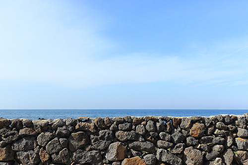 제주도에서 돌담너머로 보이는 푸른빛깔 바다의 수평선과 맞닿은 푸른하늘