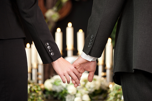 Religion, death and dolor  - couple at funeral holding hands consoling each other in view of the loss