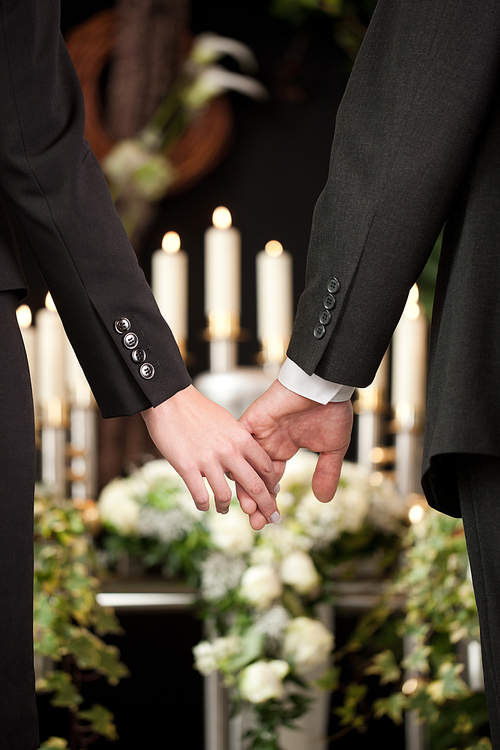Religion, death and dolor  - couple at funeral holding hands consoling each other in view of the loss