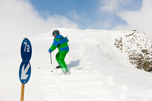 Skier walking up the hill on ski; in the front a traffic sign of the pist