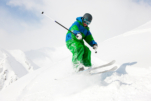 Man on a ski track going downhill, stopping in front of camera dusting some snow