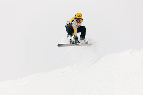 Snowboarder in the alps jumping over an edge of snow grabbing his snowboard