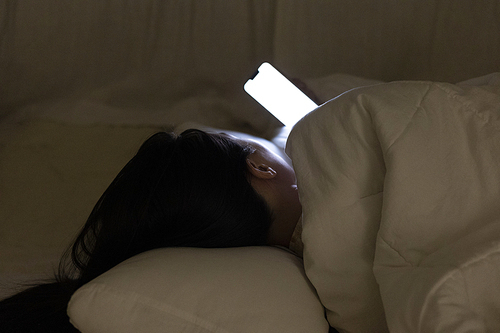 침대에 누워 이불 속에서 휴대폰을 보고 있는 여자