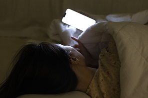 침대에 누워 이불 속에서 휴대폰을 보고 있는 여자