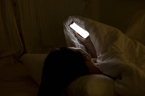 침대에 누워 이불 속에서 스마트폰을 들고 있는 여자