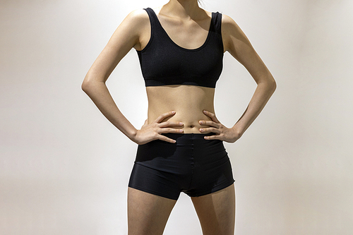 검은 스포츠웨어를 입은 슬림하고 건강한 몸매의 여성이 양팔을 골반에 대고 서있는 앞모습