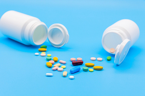 파란 배경지 위에 두개의 흰색 약병이 엎어져있고 알록달록 약들이 바닥에 엎질러진 모습의 정면사진