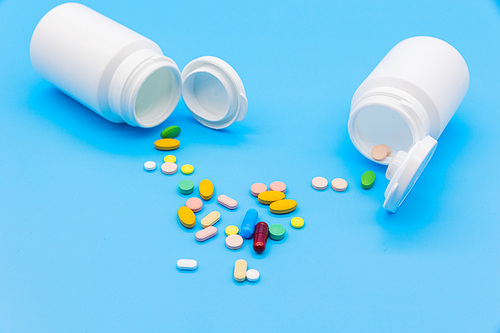 파란 배경지 위에 두개의 흰색 약병이 엎어져있고 알록달록 약들이 바닥에 엎질러진 모습