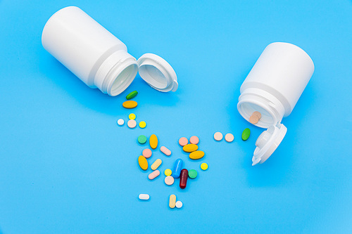 파란 배경지 위에 두개의 흰색 약병이 엎어져있고 알록달록 약들이 바닥에 엎질러진 모습의 탑뷰 사진