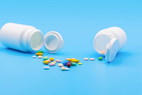 파란 배경지 위에 두개의 흰색 약병이 엎어져있고 알록달록 약들이 바닥에 엎질러진 모습의 정면사진