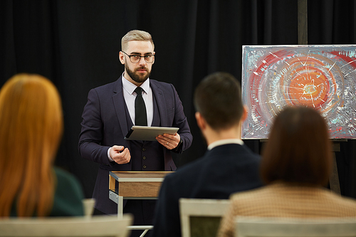 Young businessman in eyeglasses using digital tablet and performing the audience at presentation