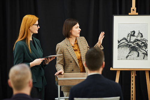 Two businesswomen standing and telling about the painting during conference