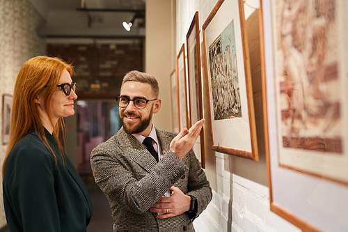 Young man pointing at picture and discussing something with young woman while they visiting art gallery