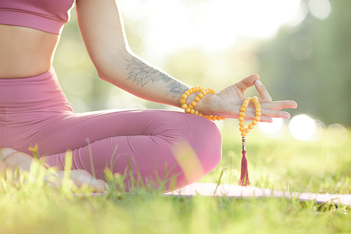 Close-up of healthy woman in pink clothing holding amulet in her hand and meditating in the park