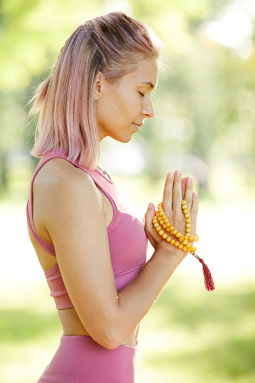 Side view of young blonde girl standing with her eyes closed and concentrating on her relaxation during yoga outdoors