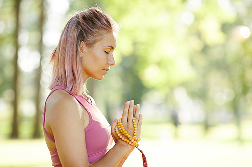 Side view of young calm woman standing with her eyes closed and listening to her mind during meditation outdoors