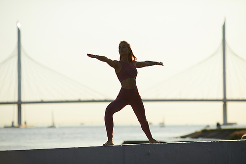 Young fit woman standing and doing stretching exercise outdoors in the city with sea in the background