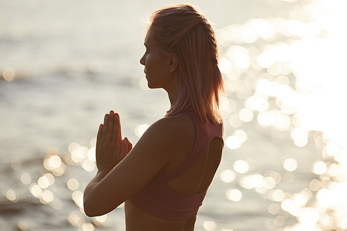 Rear view of young woman with blond hair standing with eyes closed and meditating against the beautiful sea outdoors