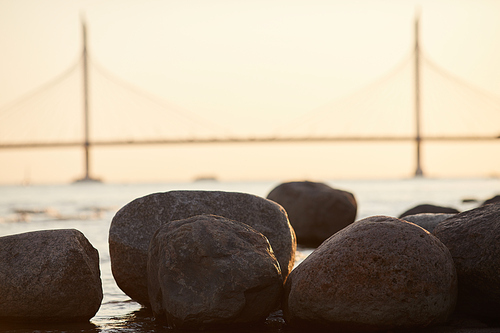 Image of big stones near the coastline of the sea in the city with big long bridge in the background