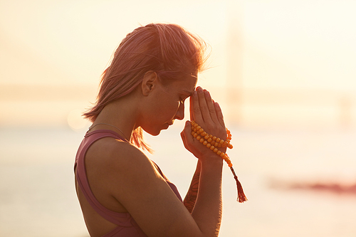Side view of young healthy woman meditating with her eyes closed during sunset in nature