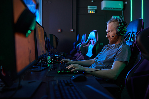 Young man wearing modern headphones sitting in front of computer monitor and typing on computer keyboard in computer class