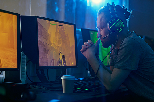 Young man in headphones sitting in front of computer monitor looking at it and thinking over the strategy of the game