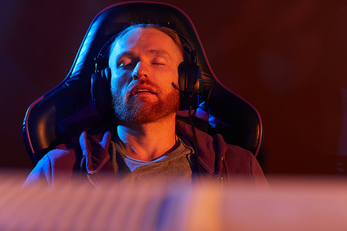 Young bearded man in headphones sitting in gaming chair and sleeping he tired after game