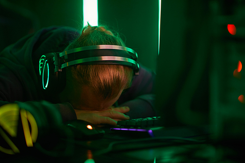 Young computer programmer in headphones lying on his table and sleeping he tired after work