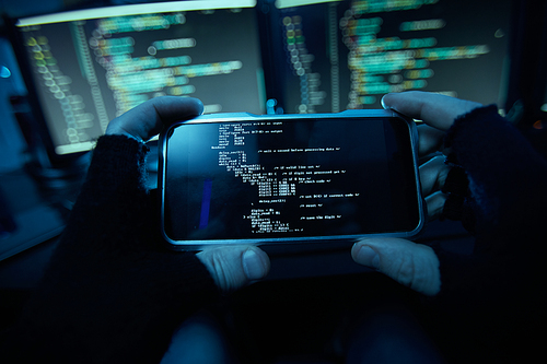 Close-up of computer hacker in black gloves holding his mobile phone and installing the new software on it in dark room