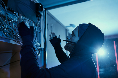 Young electrician in hoody looking at box with abundance of wires and trying to solve the problem