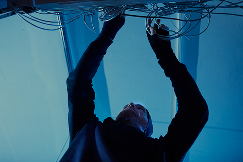 Low angle view of young man in dark clothing putting the wires in order in dark room