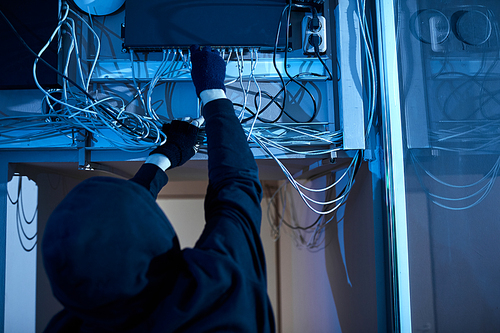 Rear view of man in hoody pulling out the wires and turning off the computers he is going to make the crime