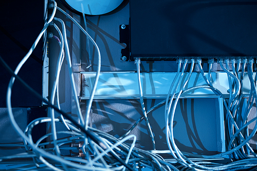 Close-up of computer system with white cables hanging on the wall in dark office