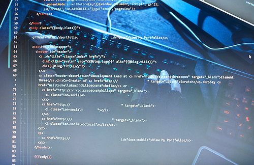 Close-up of fonts and codes on computer monitor with man typing on keyboard in the background