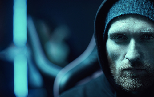 Close-up of young bearded man wearing black hoody looking at camera with serious expression