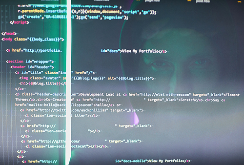 Close-up of computer monitor with codes and symbols and computer hacker reflecting on the monitor