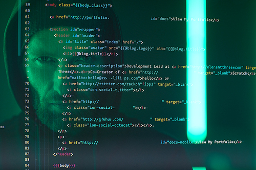 Close-up of computer screen with codes and symbols with computer hacker in black clothing in the background
