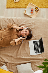 High angle view of happy girl with closed eyes lying on bed and listening to music in headphones