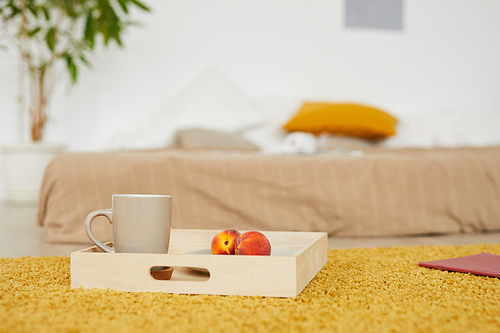 Focus on wooden tray with peaches and mug placed on yellow carpet in bedroom