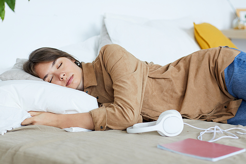 Relaxed young woman in brown shirt lying on comfortable bed and hugging soft pillow while sleeping in bedroom