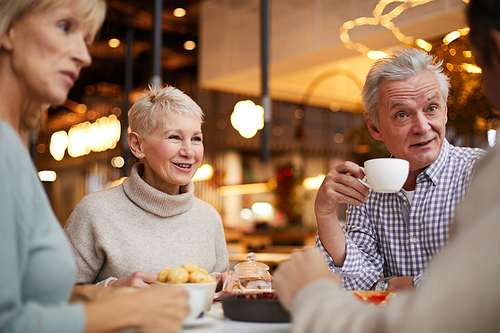 Group of positive emotional seniors sitting at table in modern cafe and chatting while drinking tea together during brunch