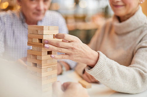 Close-up of mature woman focused on board game taking small wooden block from toy tower while playing with friends