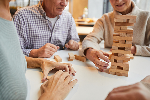 Close-up of senior board game players sitting at table and removing wooden toy blocks from tower