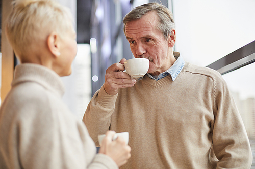 Content wrinkled senior man drinking tea and listening to woman while they spending time together