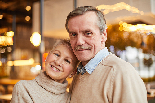 smiling beautiful mature couple in beige sweaters standing in modern restaurant and looking at .