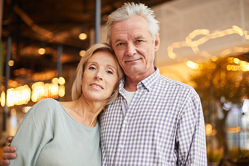Portrait of content handsome senior man with gray hair embracing beautiful wife in modern restaurant