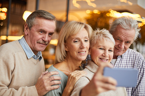 Group of smiling senior friends embracing each other while taking photo for social media
