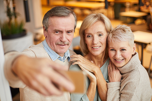 Smiling handsome man with mustache using smartphone while photographing with beautiful mature ladies
